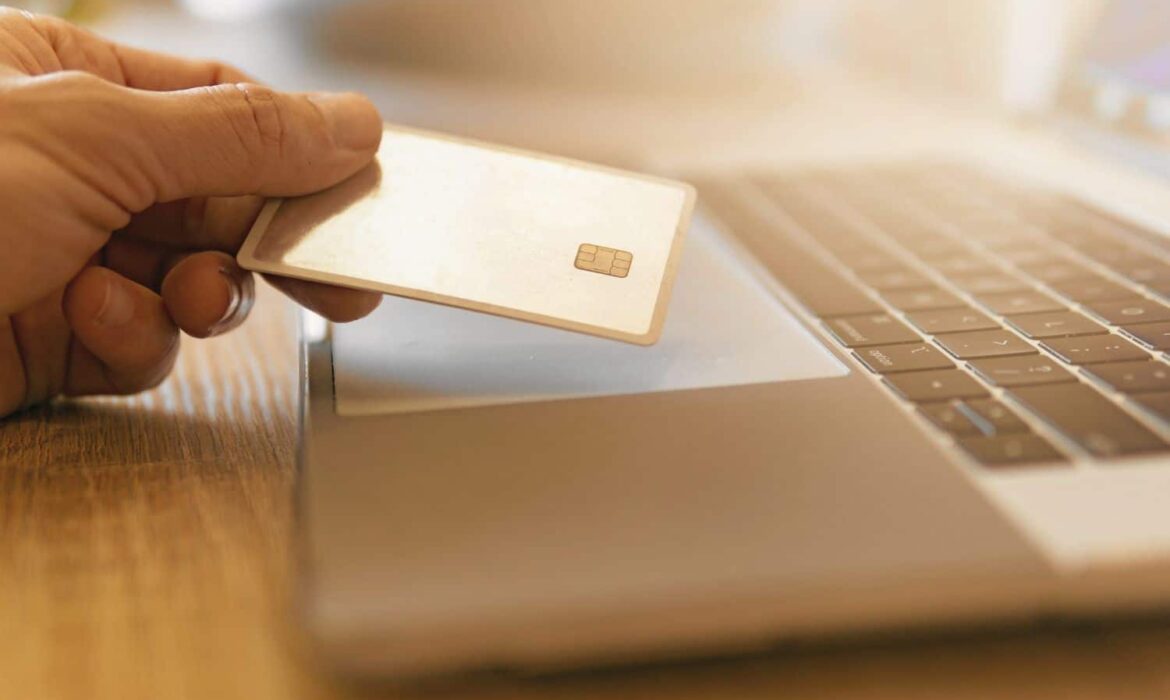 Main tenant carte bancaire au-dessus d’un ordinateur portable